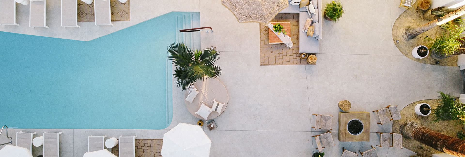 Aerial view of a modern pool area with lounge chairs, umbrellas, and tropical landscaping.