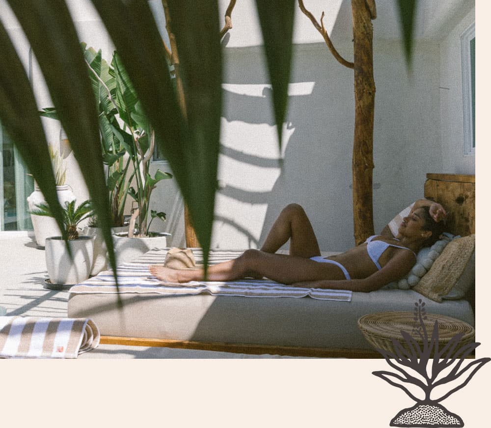 A woman in a bikini relaxes on a sunbed surrounded by tropical plants.