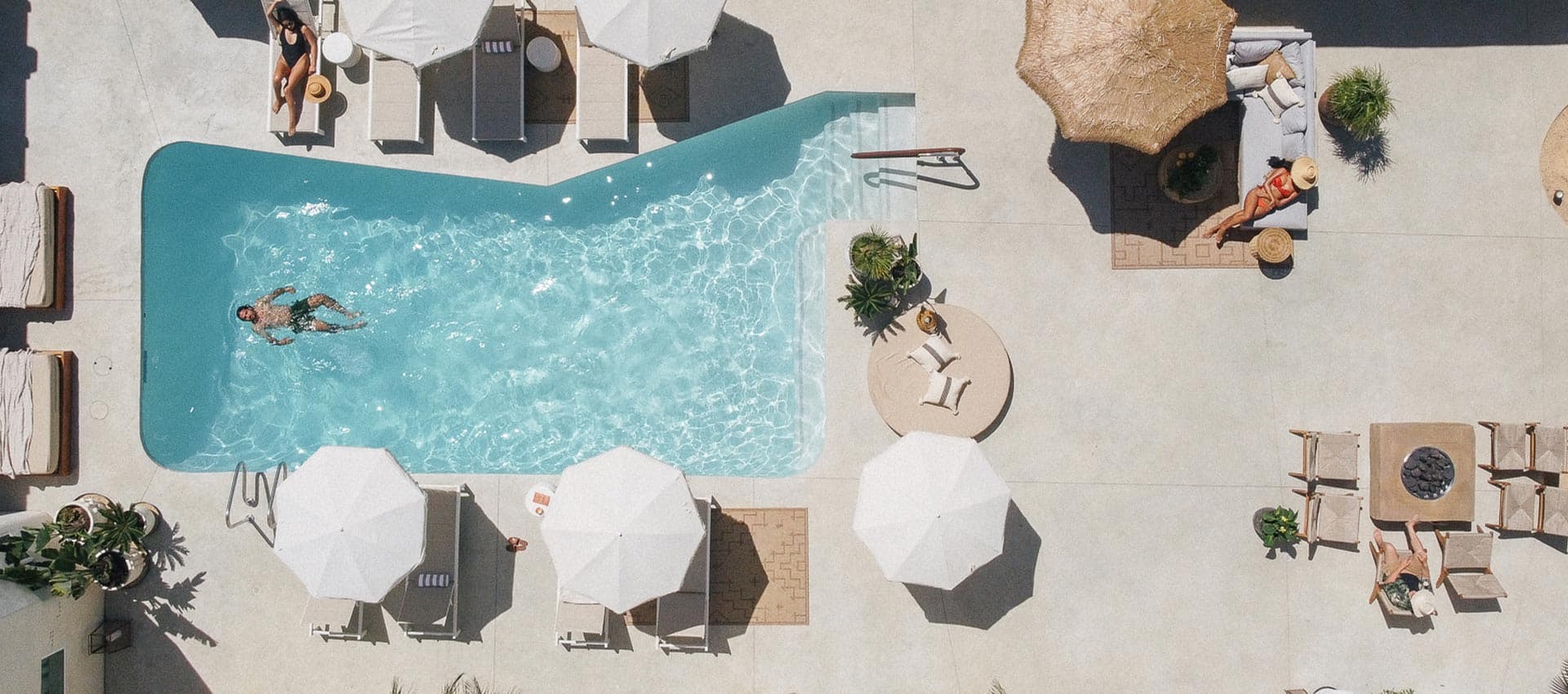 Aerial view of a pool area with sun loungers, umbrellas, and people relaxing.